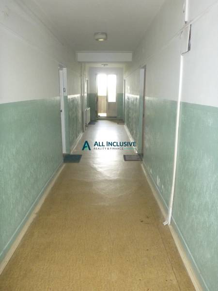 The hallway in the apartment building with light green walls leads to the balcony.