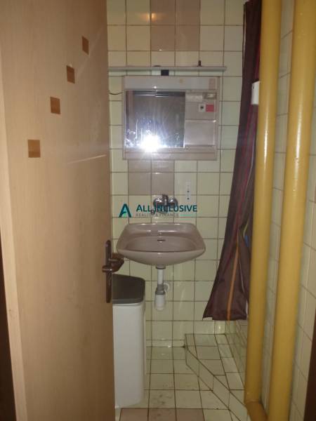 Bathroom in a studio apartment with a sink and a shower in beige tiles.