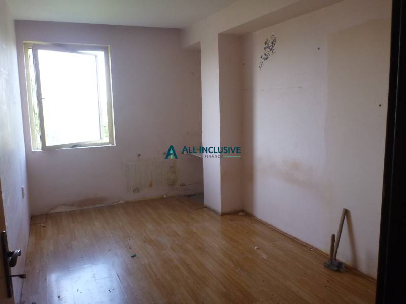 A room in a two-room apartment, pale walls, window, wooden decor flooring, slight wear.