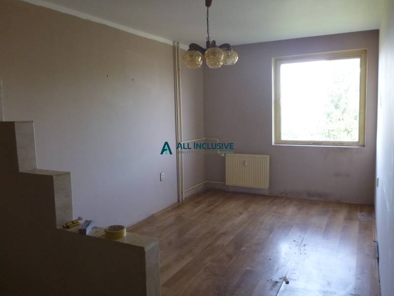 Studio apartment with wood-patterned flooring, plain walls, a window, and a chandelier.