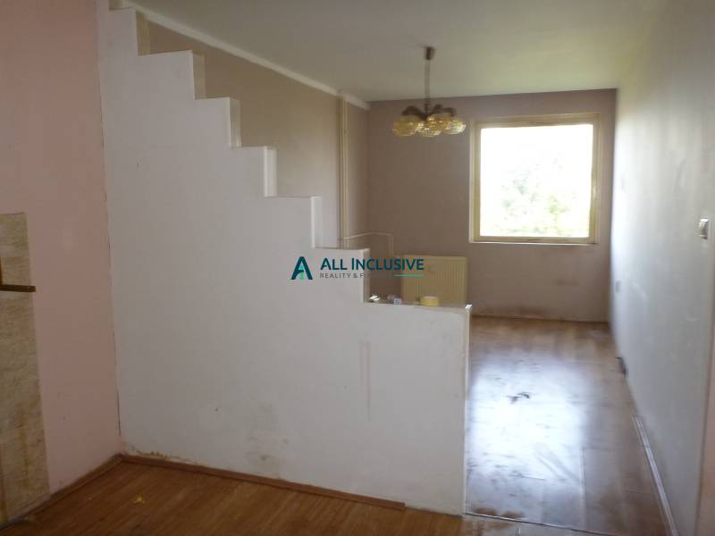 A two-room apartment with a wooden decor floor, staircase, and window offers cozy living.