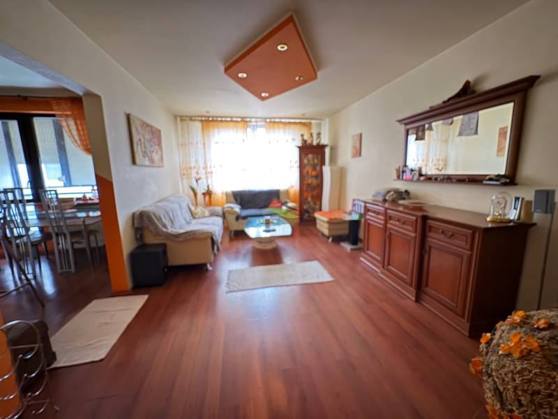 Living room in a three-room apartment with wood-patterned flooring and comfortable seating.