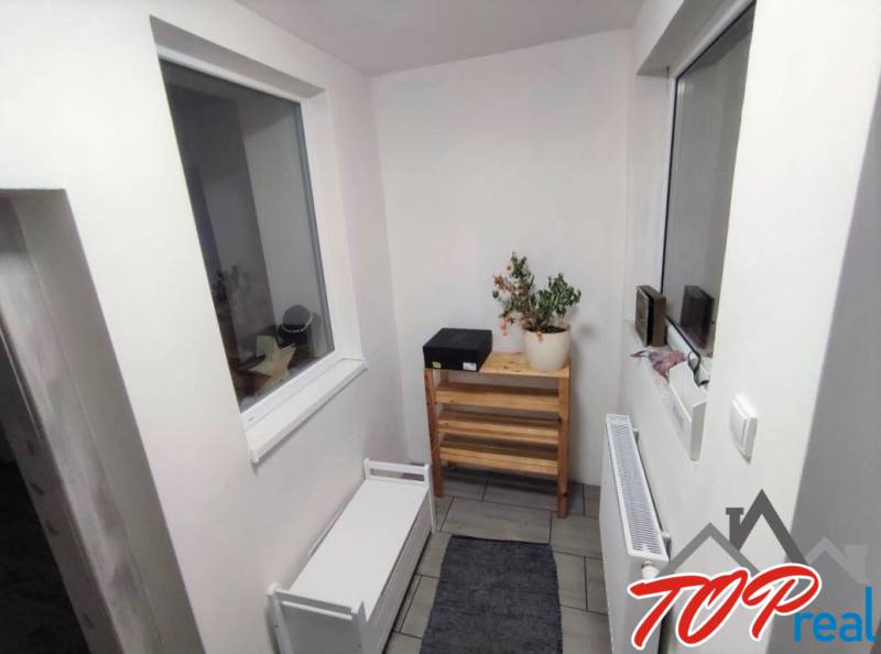 A narrow hallway with white furniture and a wooden shelf in a family house.