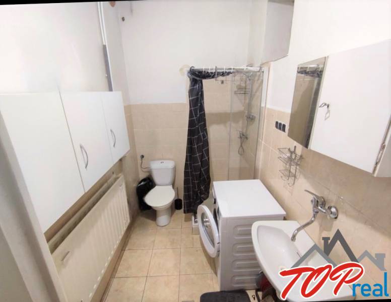 A bathroom in a family house with a shower, washing machine, and sink, with light tiles.