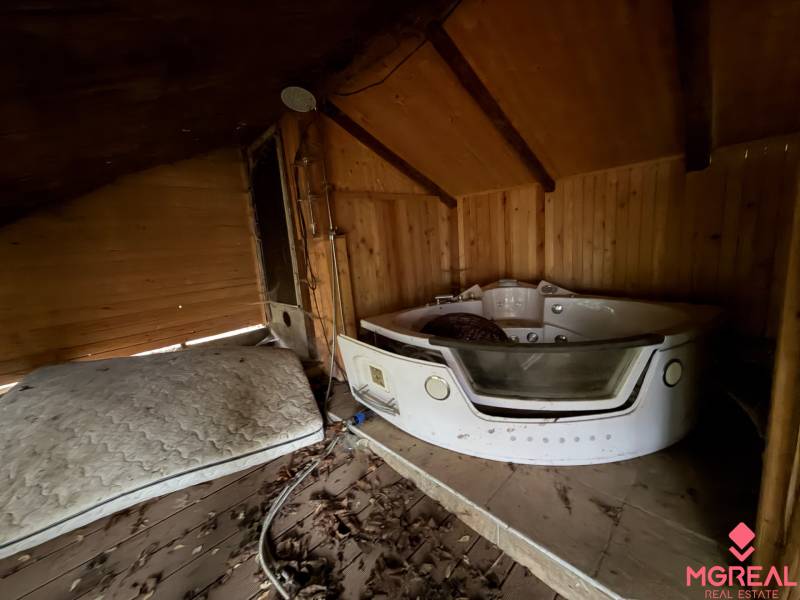 Interior of a family house with a hot tub, mattress, and wooden paneling on the walls and ceiling.