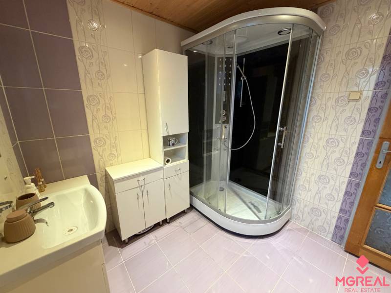 A bathroom in a family house with tiles, a shower corner, and white furniture.
