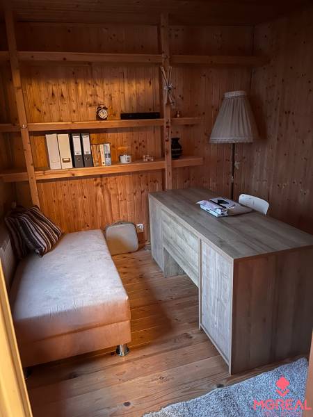 A room in a family house with wooden paneling, a sofa, a table, and shelves.