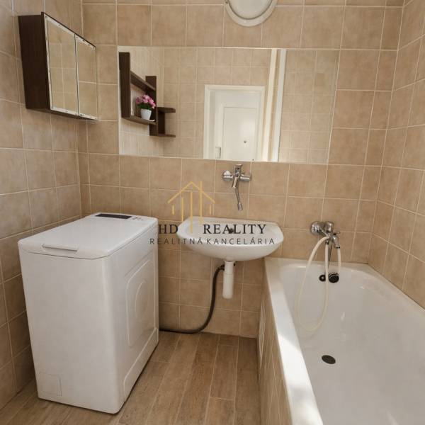 Bathroom in a studio apartment with a washing machine, bathtub, and floor with wood decor.