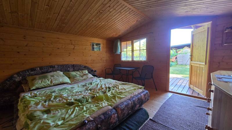 A wooden cabin with a bed, a table, and a view of the garden.