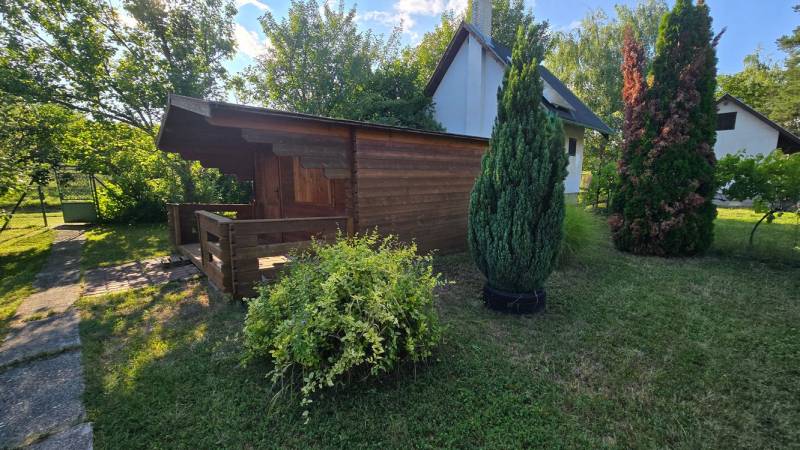 A wooden cottage in the village of Úľany nad Žitavou surrounded by green shrubs and trees.