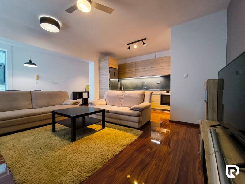 Living room in a two-room apartment with a wooden decor floor and neutral furniture.