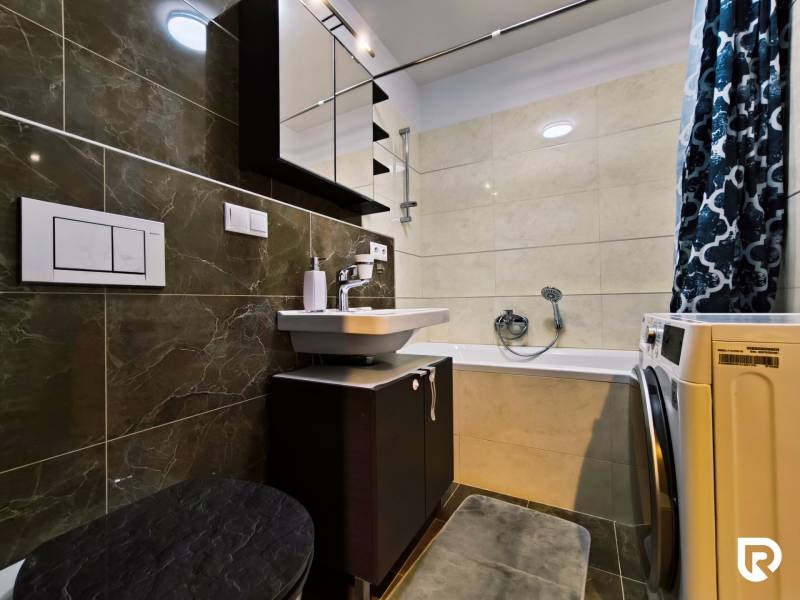 Bathroom with dark tiles, a washing machine, and a shower in a 2-room apartment.