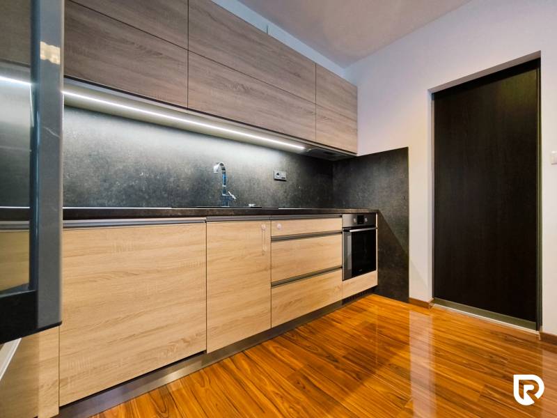 A kitchen in a 2-room apartment with wooden cabinets and a floor with a wood pattern.