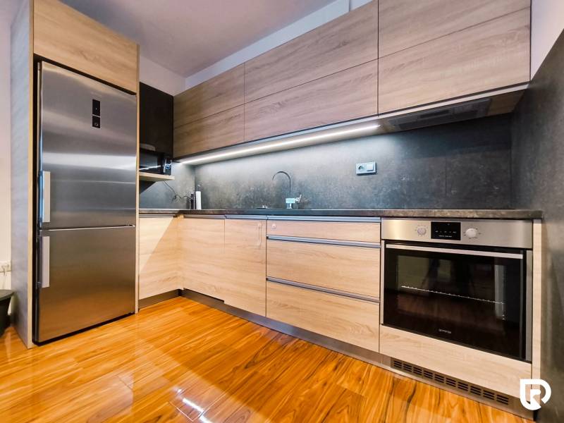 A kitchen in a 2-room apartment with a refrigerator, an oven, and a wooden decor floor.