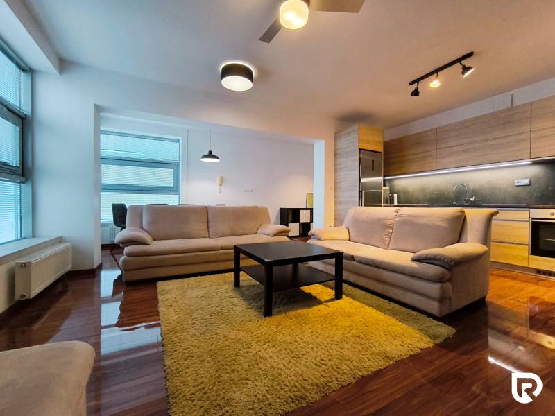 Living room in a two-room apartment with a wooden decor floor, light sofas, and a kitchen unit.