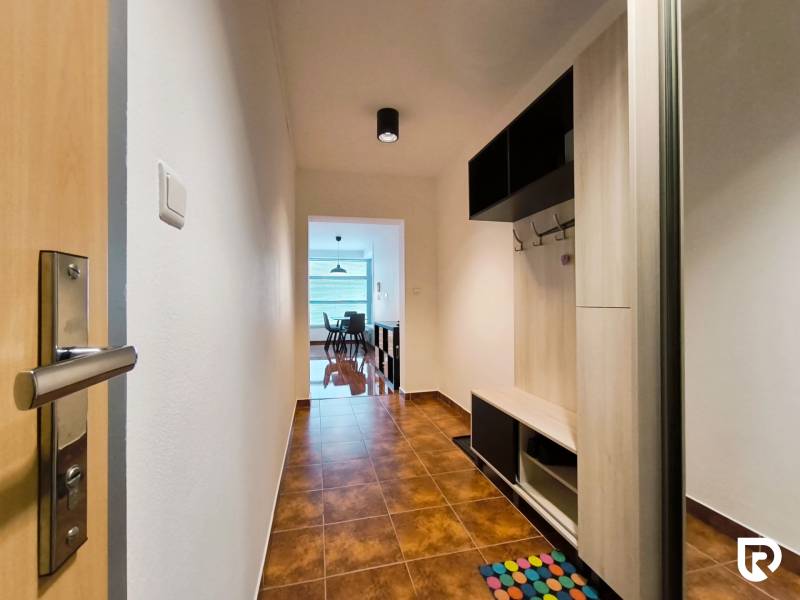 A hallway with tiles and wooden decor leads to the kitchen in a 2-room apartment.