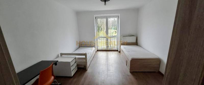 A room in a 2-room apartment with two single beds, a table, and a floor with a wooden decor.