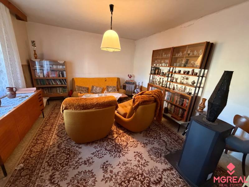 Living room in a family house with carpeted floor, seating furniture, bookshelves, and a fireplace stove.