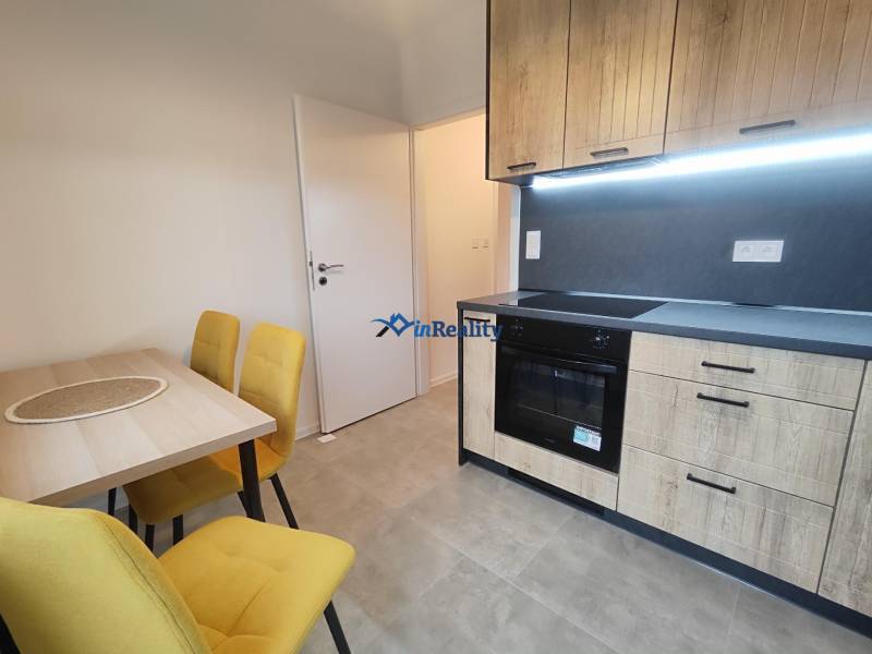 A kitchen in a studio apartment with wooden cabinets, a dining table, and yellow chairs.
