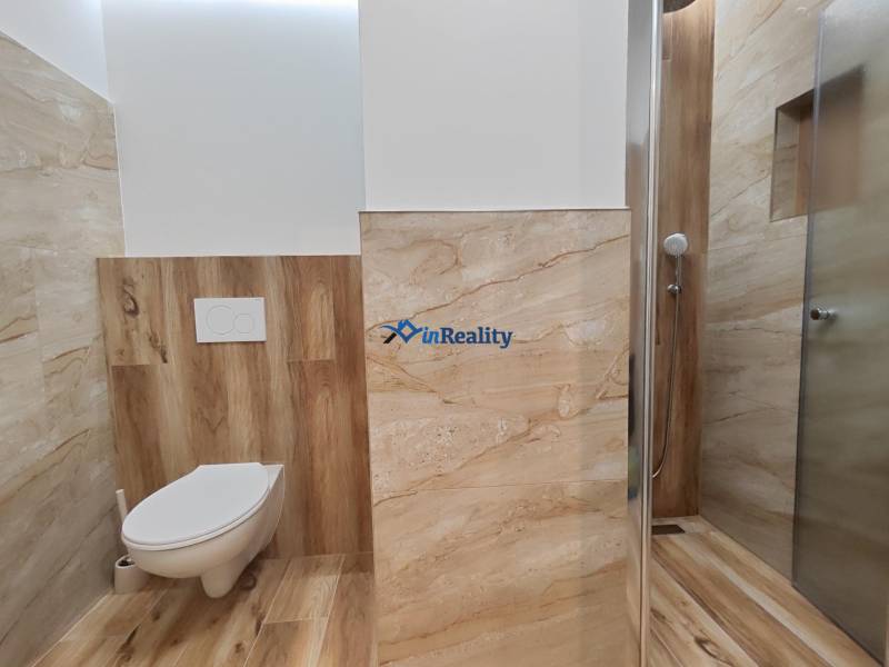 A bathroom in a studio apartment with a wooden decor floor and a shower corner.