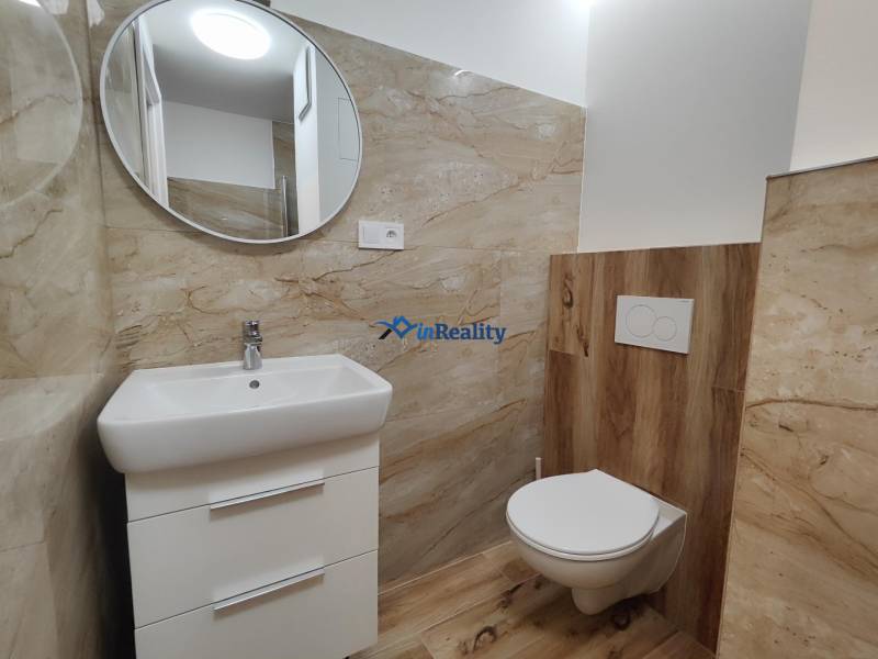 Bathroom with toilet, mirror, and light tiles in a studio apartment.