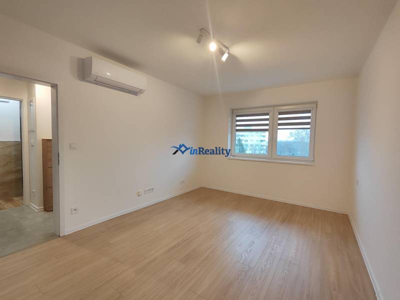 An empty room in a one-room apartment with wood-patterned flooring and air conditioning.