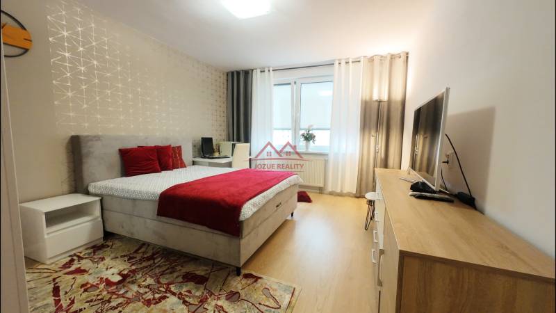 A bedroom with light furniture and red elements in a 4-room apartment with a wooden decor floor.