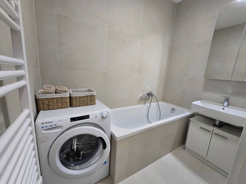 A bathroom with a bathtub, sink, and washing machine in a 3-room apartment.