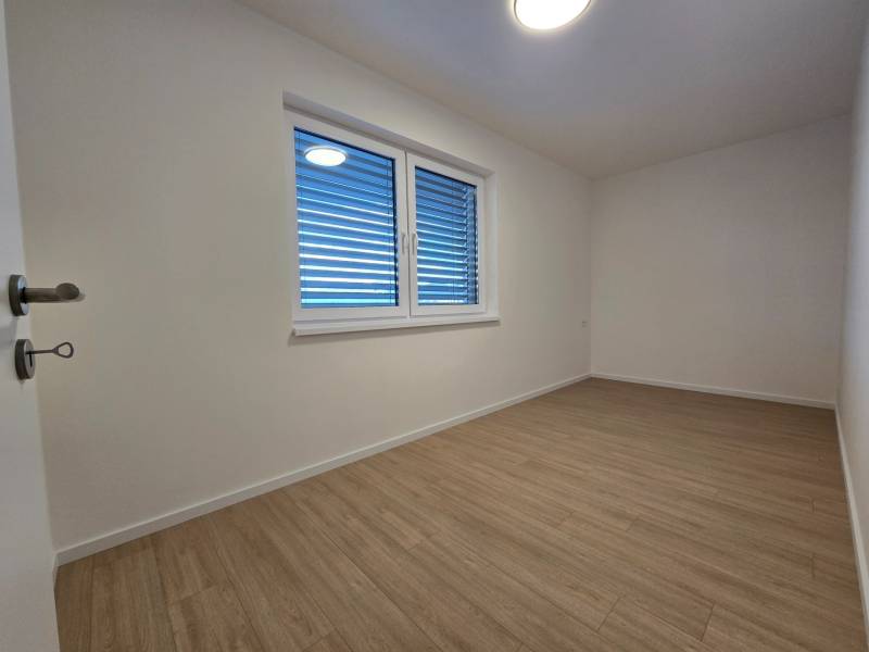 A room in a 3-room apartment with a wooden decor floor and a window with blinds.