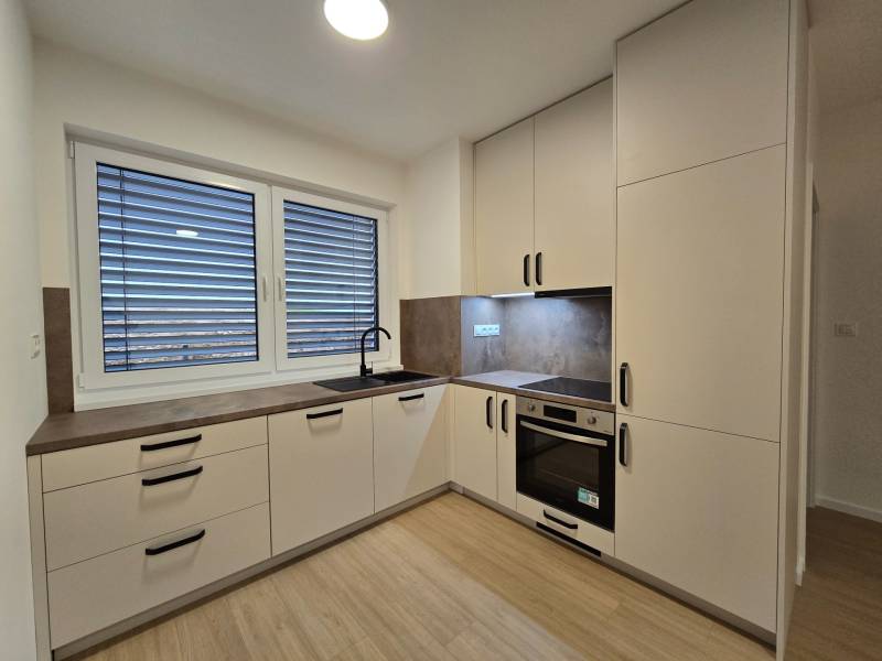 A kitchen with a wooden decor floor in a 3-room apartment, light cabinets, and built-in appliances.