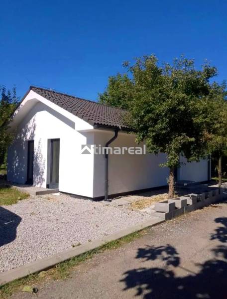 A family house in Kaplna with a white facade, a sloped roof, and greenery around.
