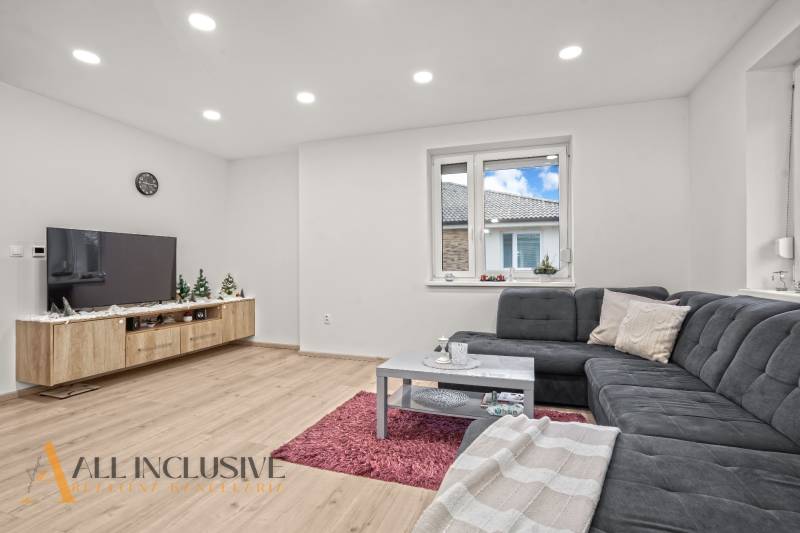 Living room with a corner sofa, wooden decor flooring, and a television in a three-room apartment.