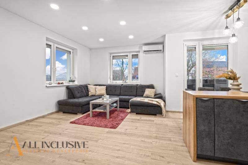 Living room of a three-room apartment with a wooden decor floor, comfortable seating, and large windows.