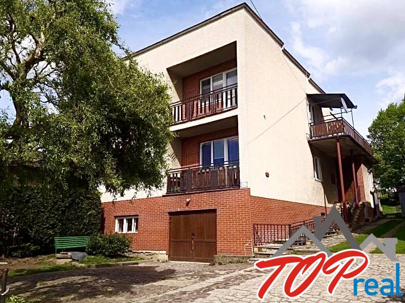 A family house in Nižná Myšľa with balconies, a tree, and a garage on a paved area.