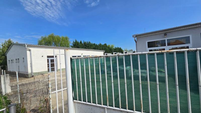 The white building in Šaľa is part of Warehouses and Halls, surrounded by a fence and greenery.