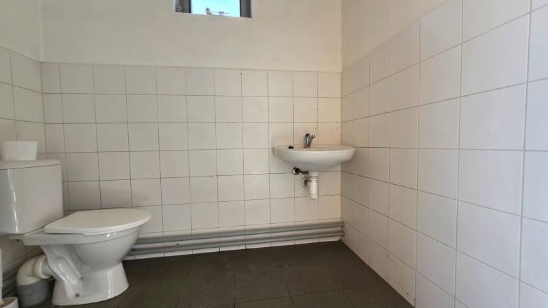 A restroom in warehouses and halls with white tiles and a small window.