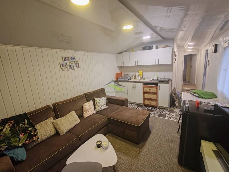 Living room in a cottage with a comfortable sofa, kitchen unit, and decorative wall cladding.