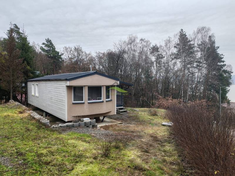 A wooden cottage on Main Street in Nova Kelca surrounded by trees and a grassy plot.