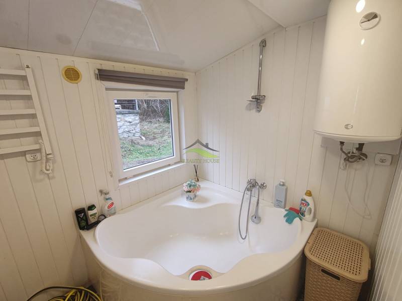 A bathroom in the cottage shows a bathtub, a boiler, and a small window with a view.