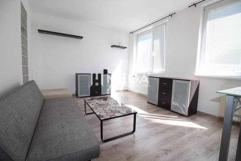 Living room in a two-room apartment with a sofa, glass table, and wooden decor flooring.