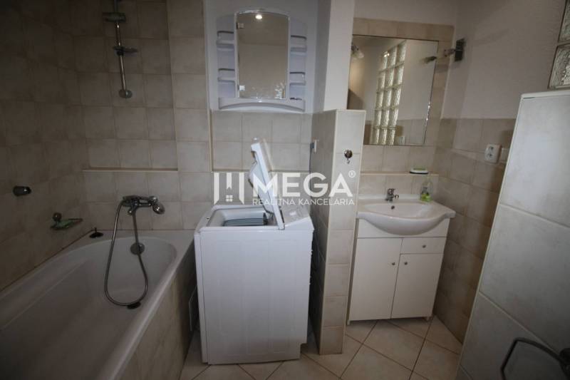 Bathroom with a bathtub, washing machine, sink, and mirror in a 2-room apartment.