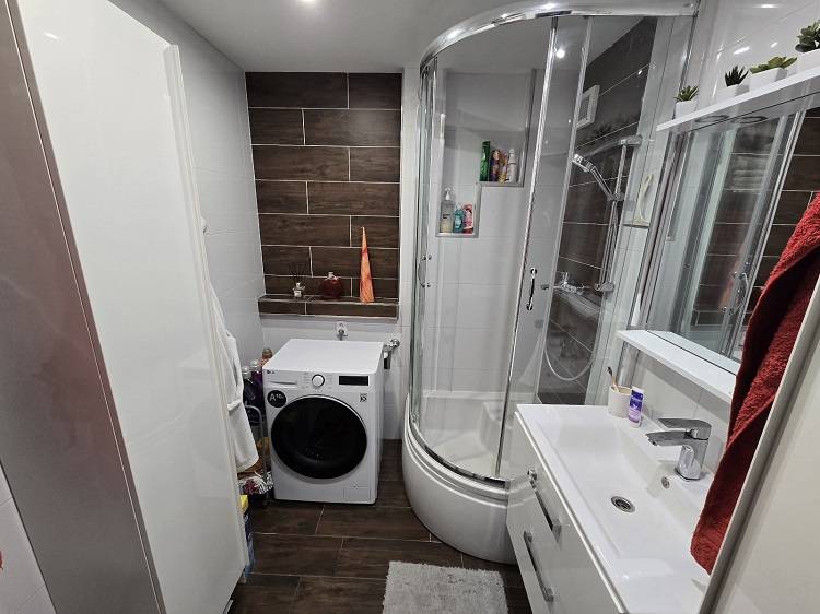 A bathroom with a washing machine, shower cabin, and modern tiles in a 3-room apartment.