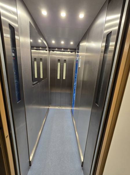 Illuminated interior of an elevator with metal walls and a blue floor.