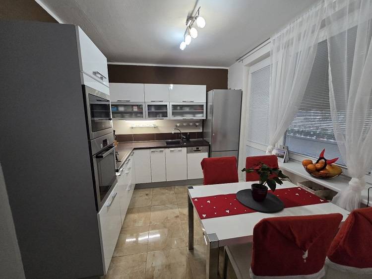 A kitchen in a 3-room apartment with glossy white cabinets, appliances, and a dining table.