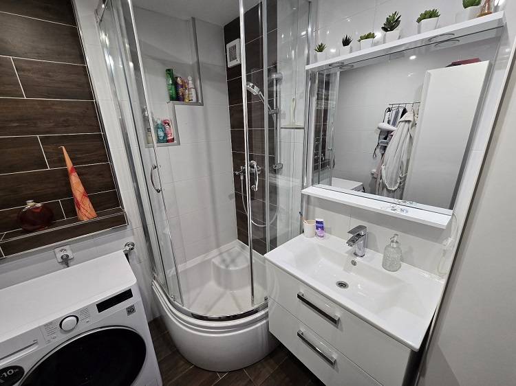 A bathroom in a 3-room apartment with a washing machine, shower, and sink.