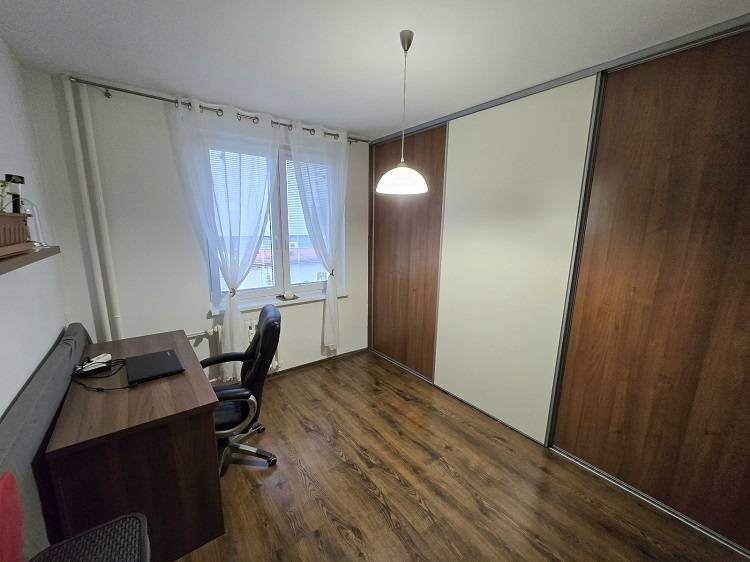 A room in a 3-room apartment with a desk and a floor with a wood decor.