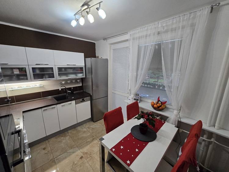 A kitchen in a 3-room apartment with white furniture, a dining table, and a floor with a wood decor.