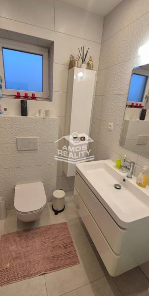 A bathroom in a family house with white tiles, a sink, and a toilet, complemented by decorations.