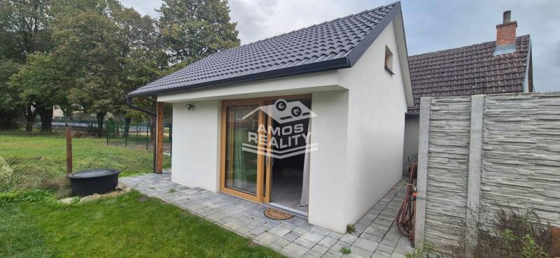 A family house in Studienka with a white facade and a sloped roof, framed by green trees.