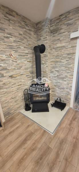 A wood-burning fireplace in the corner of the room with stone cladding and a wooden decor floor.
